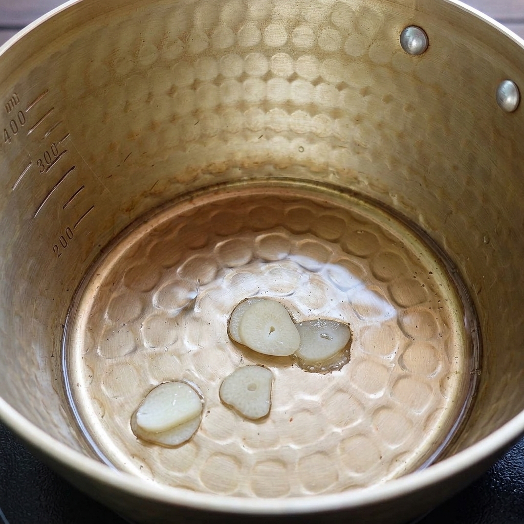 Láminas de ajo friéndose suavemente en manteca de cerdo líquida.