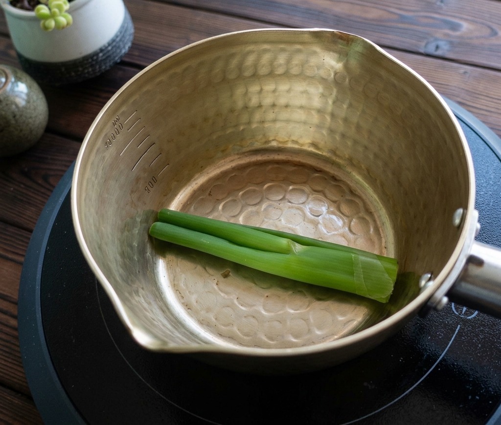 Tallos de cebolleta verde en el fondo de una olla metálica.