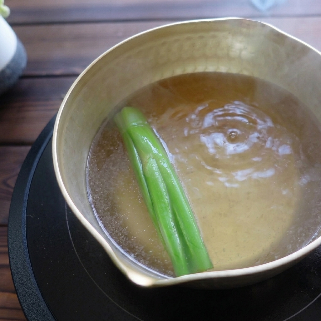 Caldo de ramen hirviendo suavemente con cebolletas en una olla.
