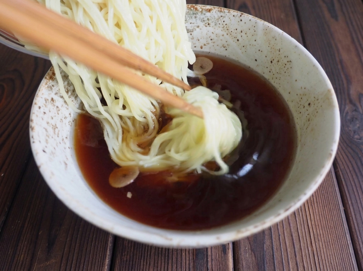 Palillos colocando fideos ramen en el cuenco con caldo oscuro.