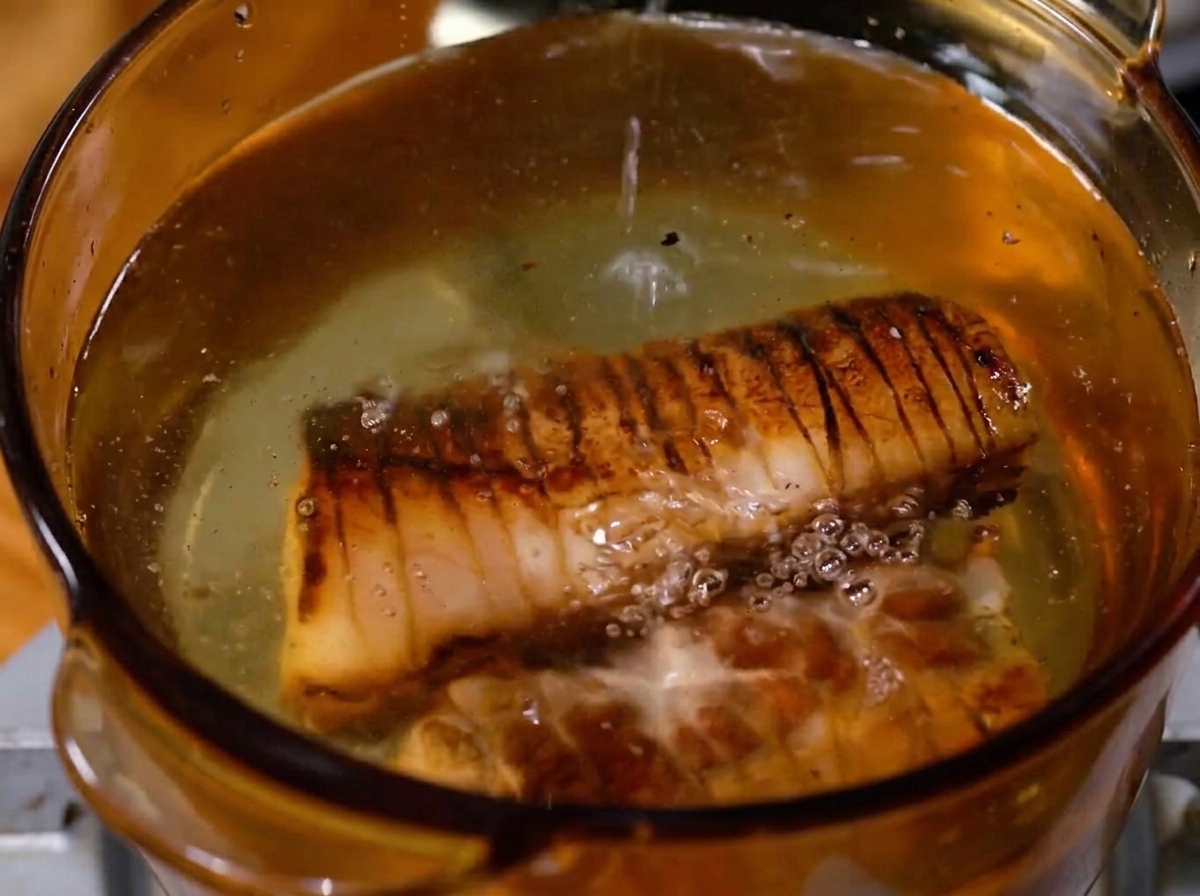 Panceta sellada hirviendo en una olla con líquido y aromáticos.
