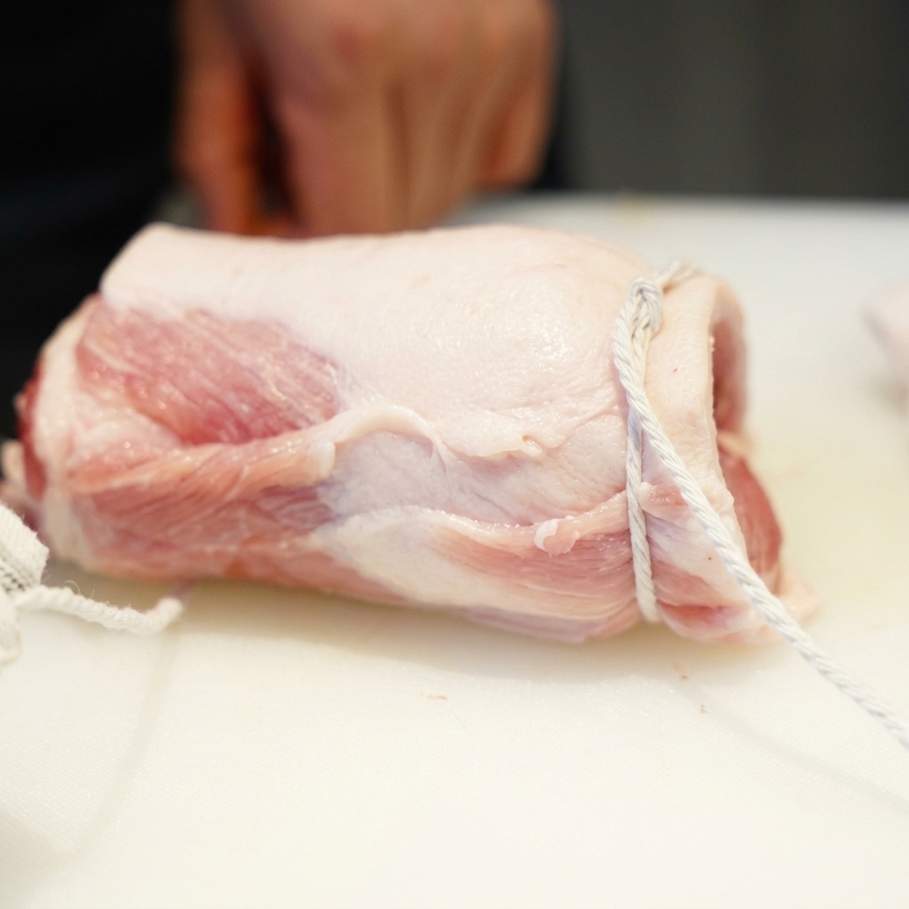 Panceta de cerdo cruda enrollada firmemente en un cilindro y atada con hilo blanco de cocina.