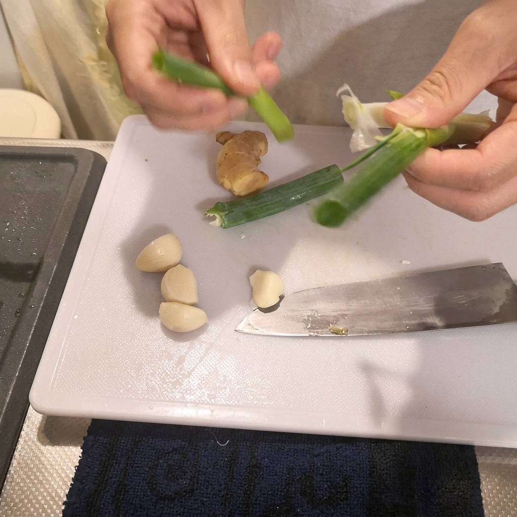 Manos preparando cebolletas verdes sobre una tabla de cortar blanca junto a un cuchillo de cocina.