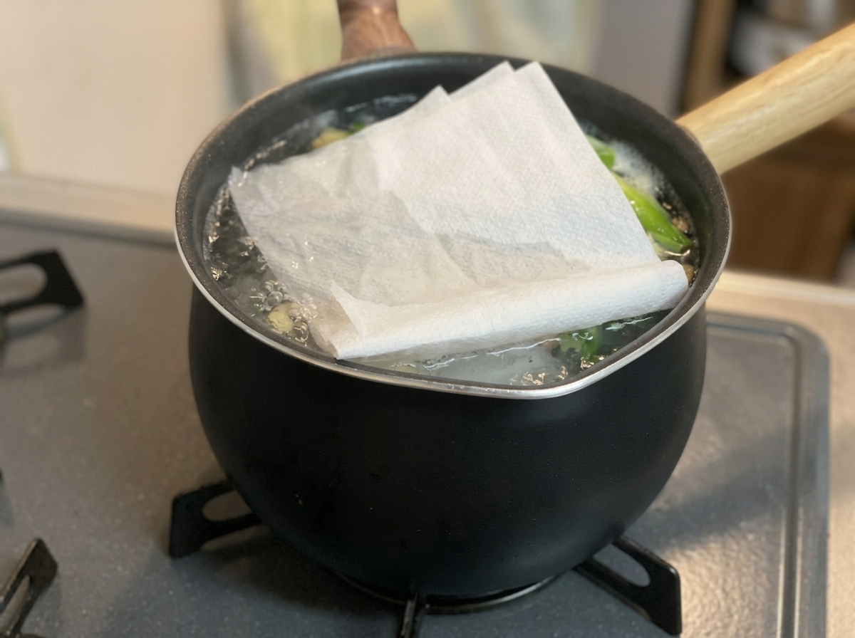 Una toalla de papel blanca doblada colocada sobre la superficie de un caldo burbujeante en una olla negra en una estufa.