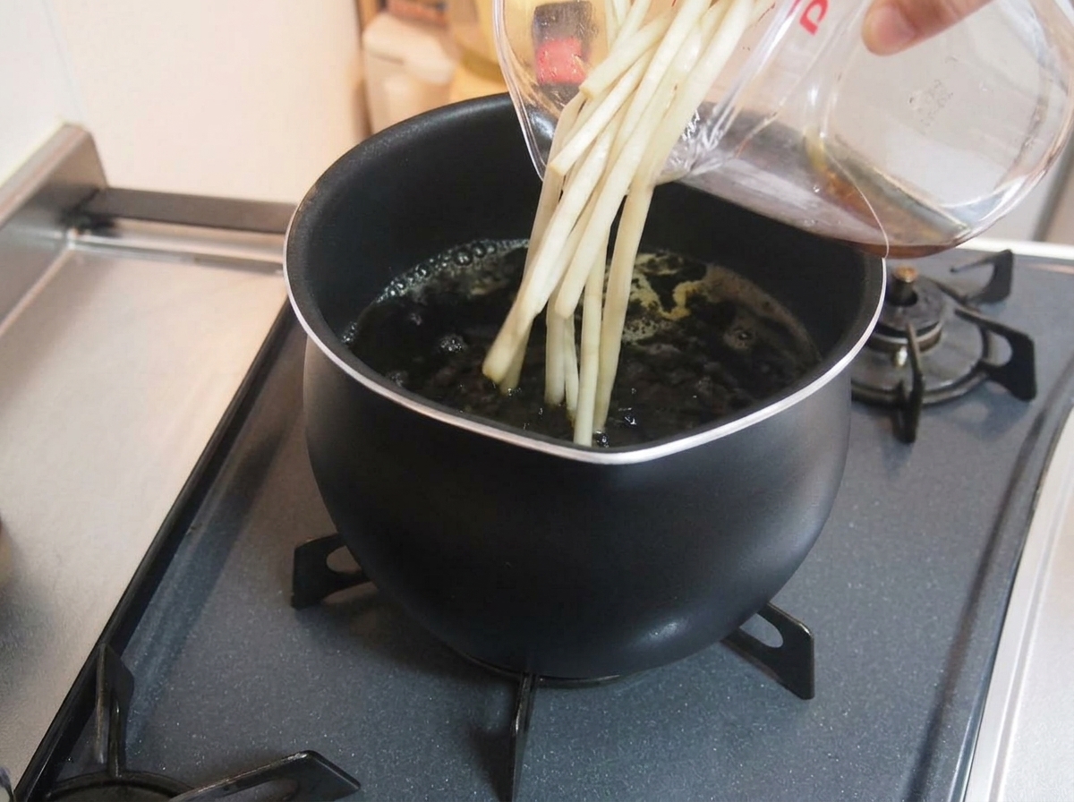Vertiendo líquido y aromáticos desde una taza medidora transparente a una olla hirviendo a fuego lento con caldo oscuro.