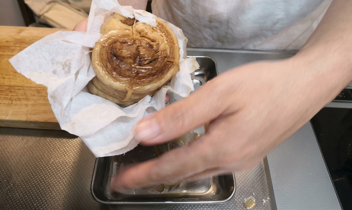 Manos usando una toalla de papel para secar con palmaditas un rollo de panceta de cerdo estofada sobre una bandeja de metal.