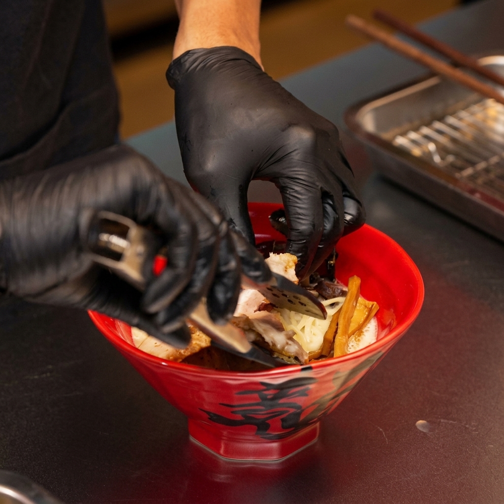 Manos usando pinzas para colocar el cerdo chashu braseado en el bol de ramen miso.