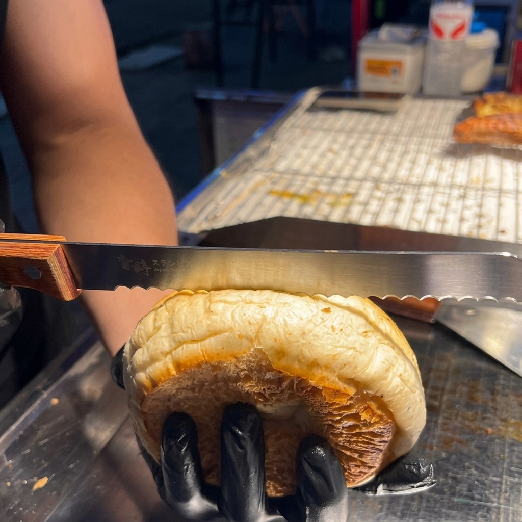 Una mano usando un cuchillo de sierra para cortar suavemente un pan de hamburguesa con sésamo por la mitad horizontalmente.