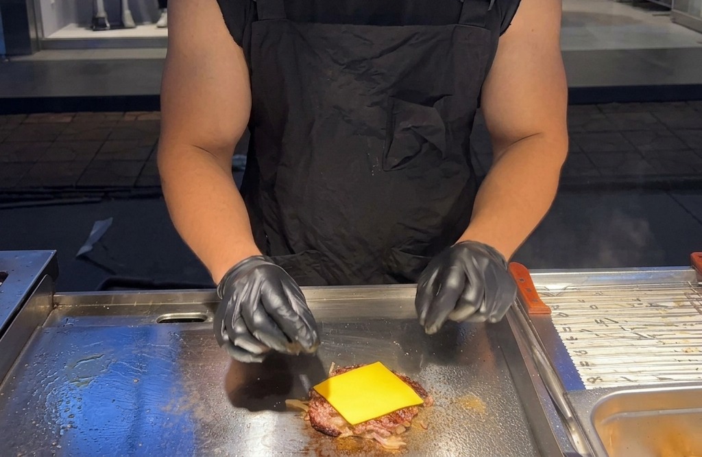 Una loncha cuadrada de queso americano amarillo colocada sobre una hamburguesa de carne caliente en una plancha.