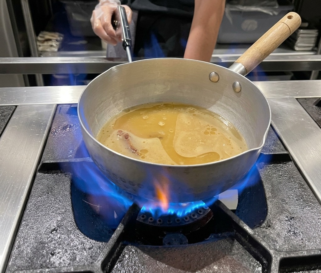 Una olla metálica con caldo de ramen de miso hirviendo suavemente sobre una llama azul de gas.