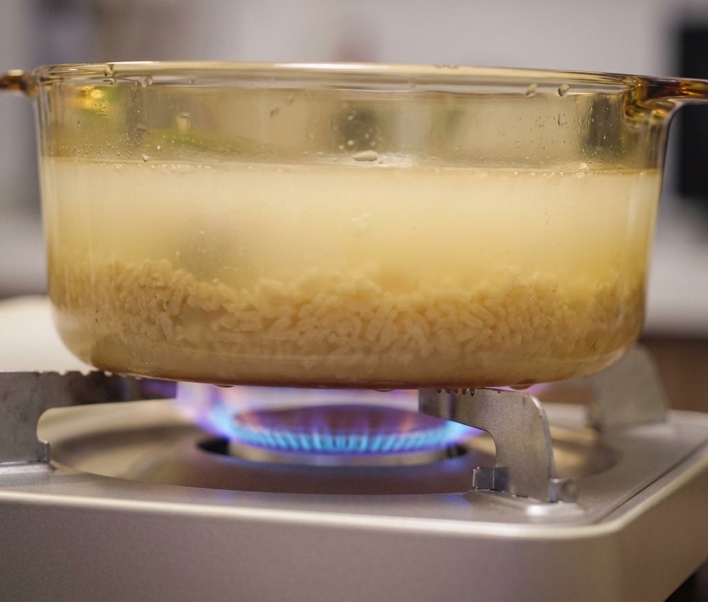 Olla de vidrio con caldo de ramen hirviendo suavemente sobre una llama de gas azul.