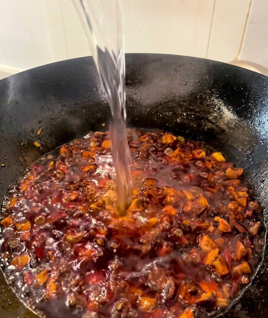 Un chorro de agua clara vertiéndose en un wok con salsa de pollo y setas que hierve suavemente.