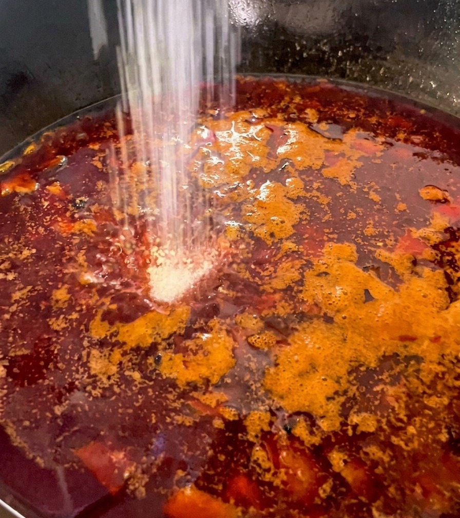 Condimento blanco espolvoreado sobre un caldo rojo burbujeante con setas y pollo.