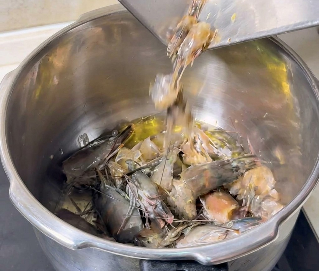 Cabezas y cáscaras de gamba vertiéndose en una olla con aceite caliente para freír.