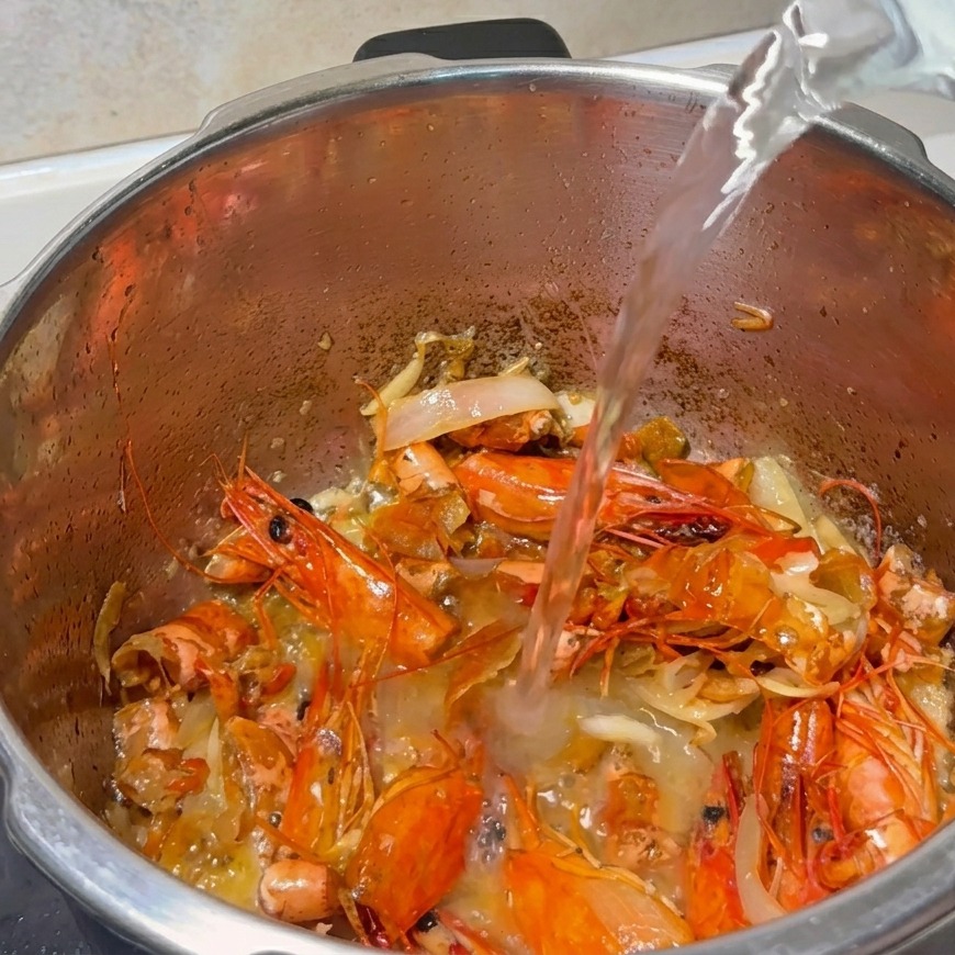 Un chorro de agua vertiéndose en la olla con cáscaras de gamba y aromáticos.