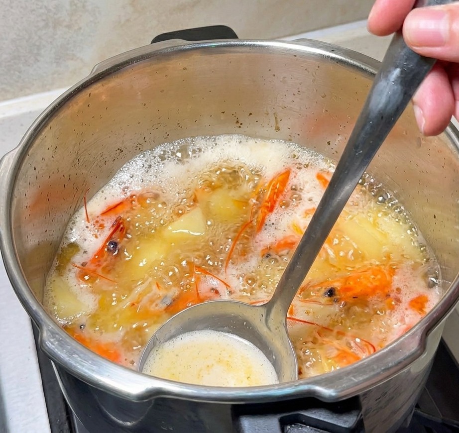 Un cucharón removiendo un caldo naranja burbujeante con cabezas de gamba y mantequilla derritiéndose.