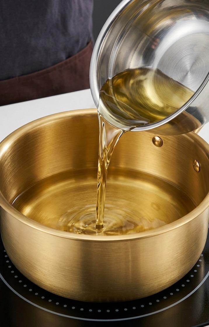Aceite de cacahuete y aceite de sésamo calentándose en una olla dorada sobre una placa de inducción.
