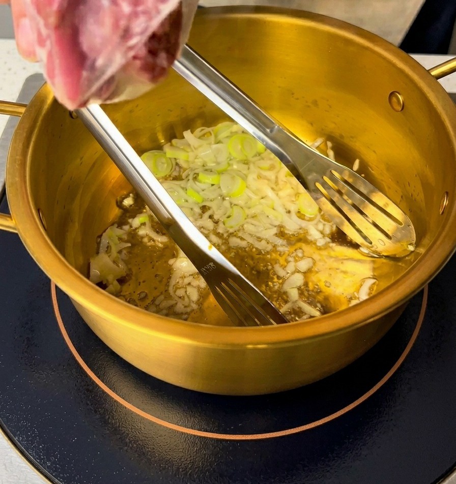Cebolletas verdes cortadas y ajo picado sofriéndose en aceite al fondo de una olla dorada.