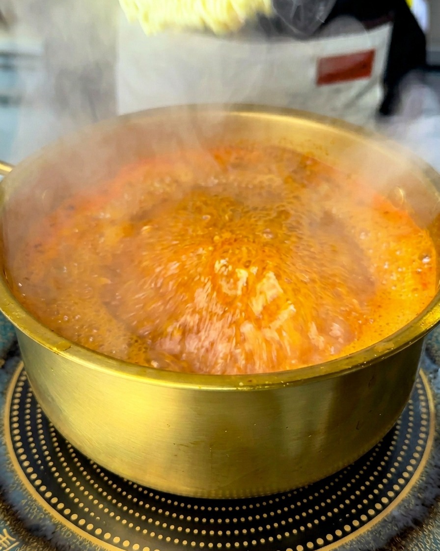 Bloque de fideos ramen instantáneos sumergiéndose en una olla de sopa roja hirviendo.