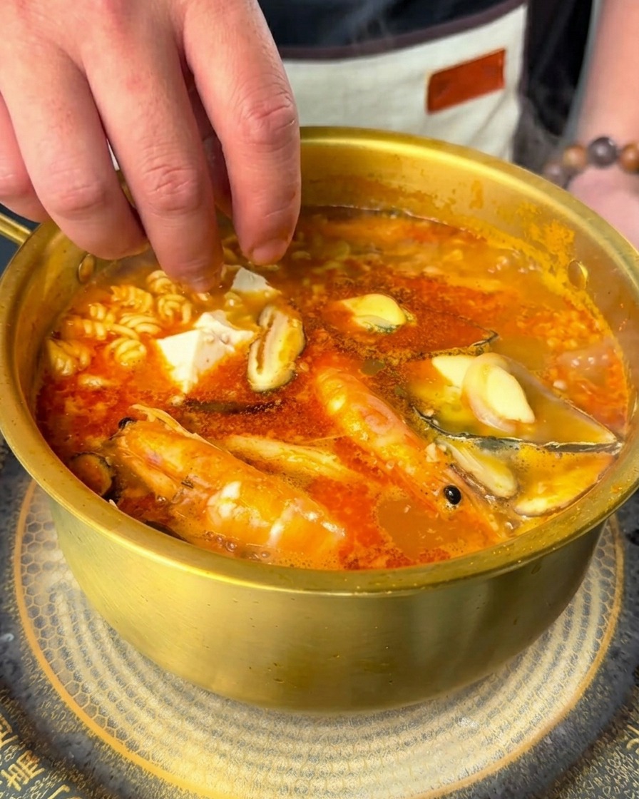 Mano dejando caer cubos de tofu suave y rodajas de chile fresco en el ramen hirviendo.