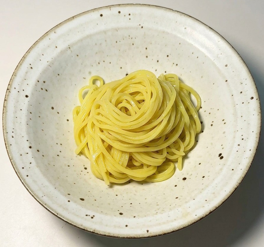 Un nido ordenado de fideos ramen amarillos centrado en un bol de cerámica blanca moteada.