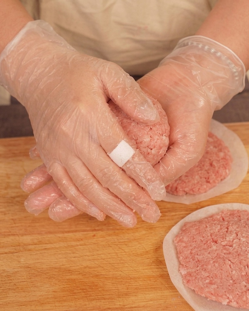 Una persona con guantes de plástico lanzando una bola de carne picada entre sus manos sobre una tabla de madera.