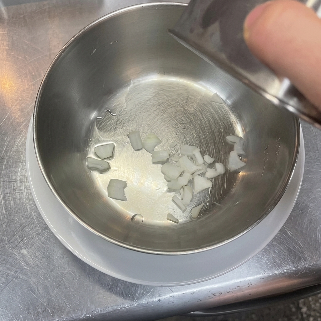 Pequeños trozos de cebolla blanca picada en el fondo de un bol para mezclar de acero inoxidable limpio.