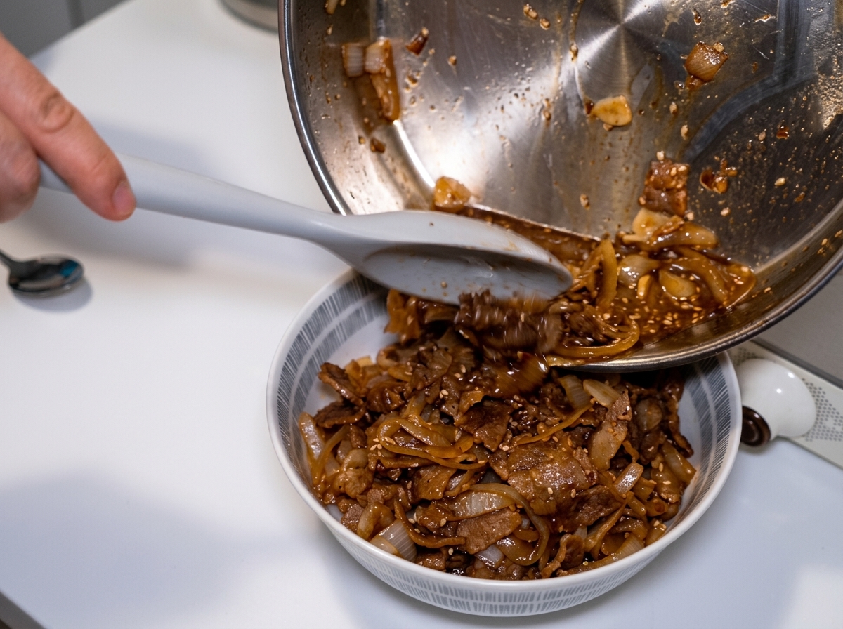 Inclinando una sartén y usando una espátula para verter las cebollas restantes y la rica salsa oscura sobre un tazón de arroz con ternera.