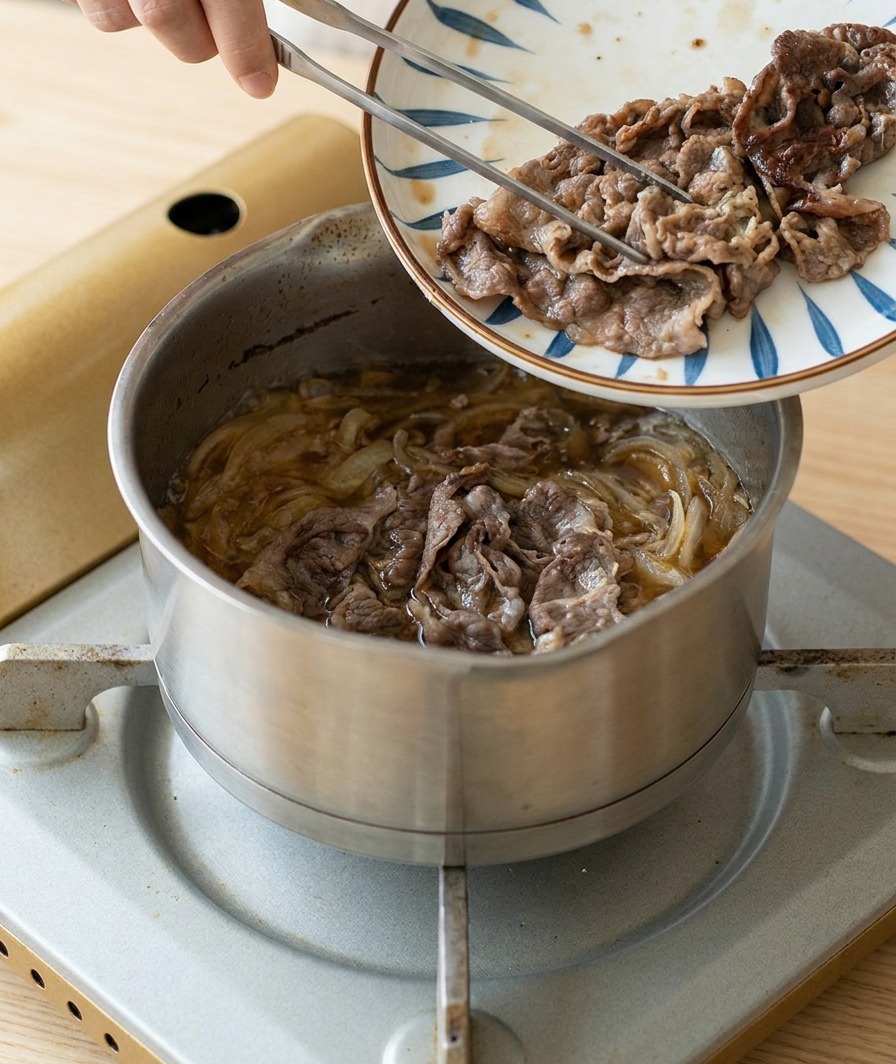 Láminas de carne dorada y sellada pasándose desde un plato decorado hacia una olla con cebollas y salsa hirviendo a fuego lento.