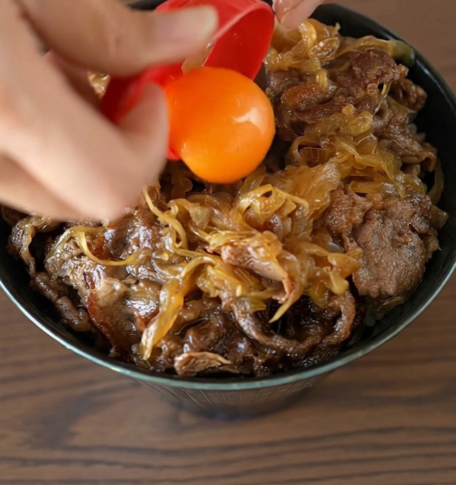 Una yema de huevo de color naranja brillante cayendo desde un separador rojo justo en el centro de un tazón de carne terminado.