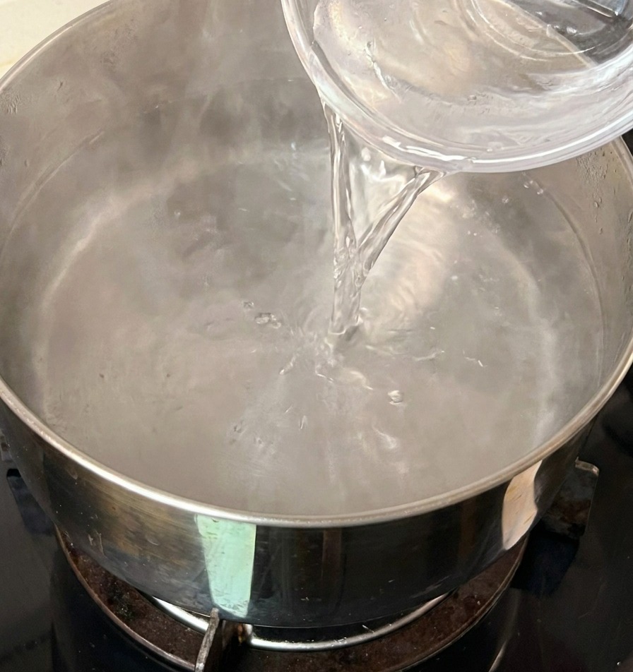Vertiendo un pequeño cuenco de agua fría en una olla de acero inoxidable con agua caliente.