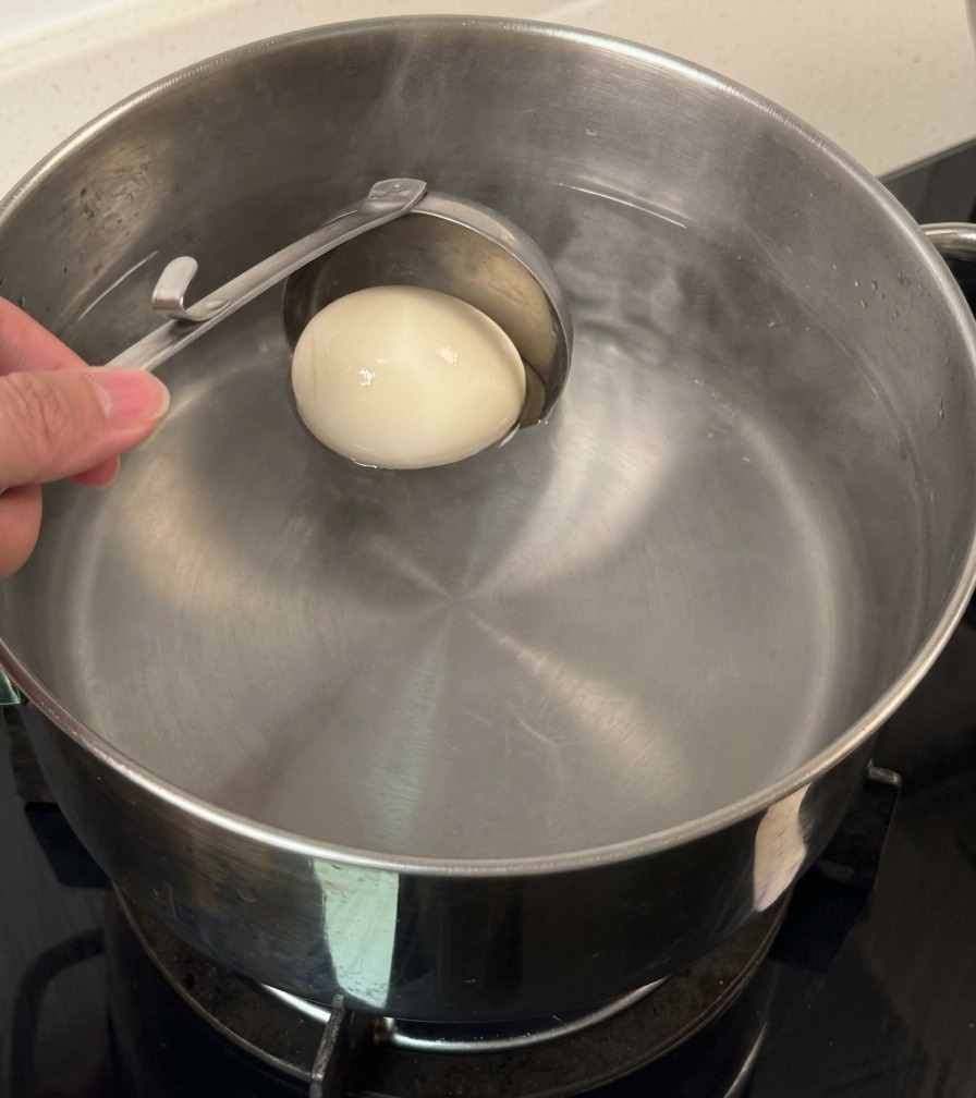 Un cucharón metálico introduciendo un huevo entero en una olla con agua.