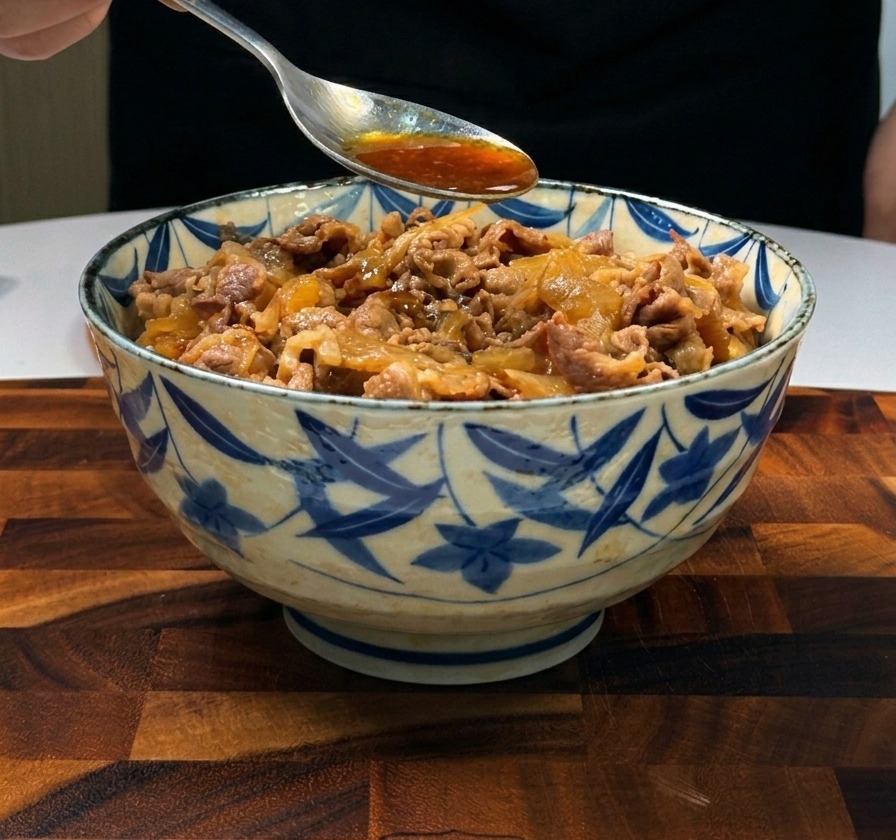 Una cuchara metálica vertiendo salsa marrón sabrosa sobre láminas de ternera y cebolla servidas sobre arroz blanco.
