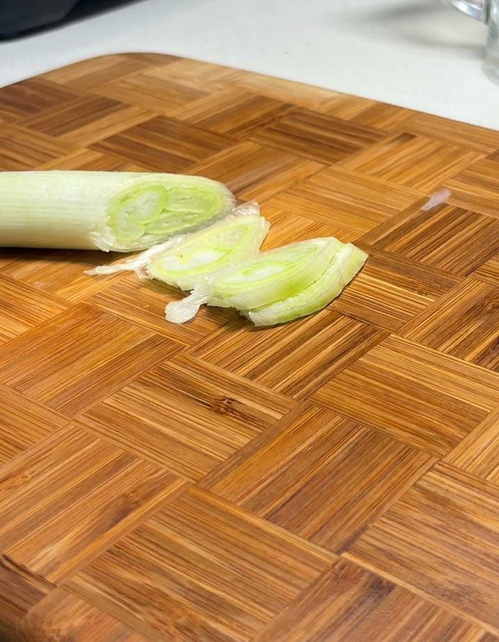 Cebolletas verdes cortadas en diagonal dispuestas sobre una tabla de cortar de madera.