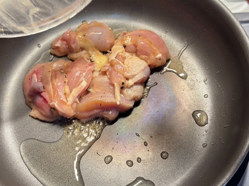 Trozos de pollo marinado sellándose en una sartén caliente con una ligera capa de aceite.