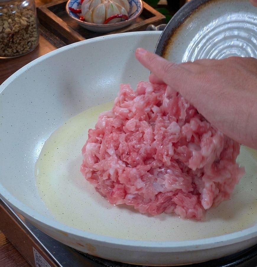 Carne de cerdo picada fresca colocada en una sartén de cerámica blanca con una ligera capa de aceite.