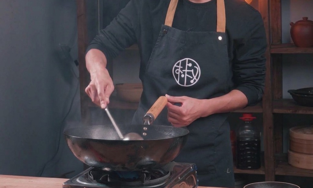 Un chef salteando carne picada en un wok tradicional mientras añade los condimentos líquidos.