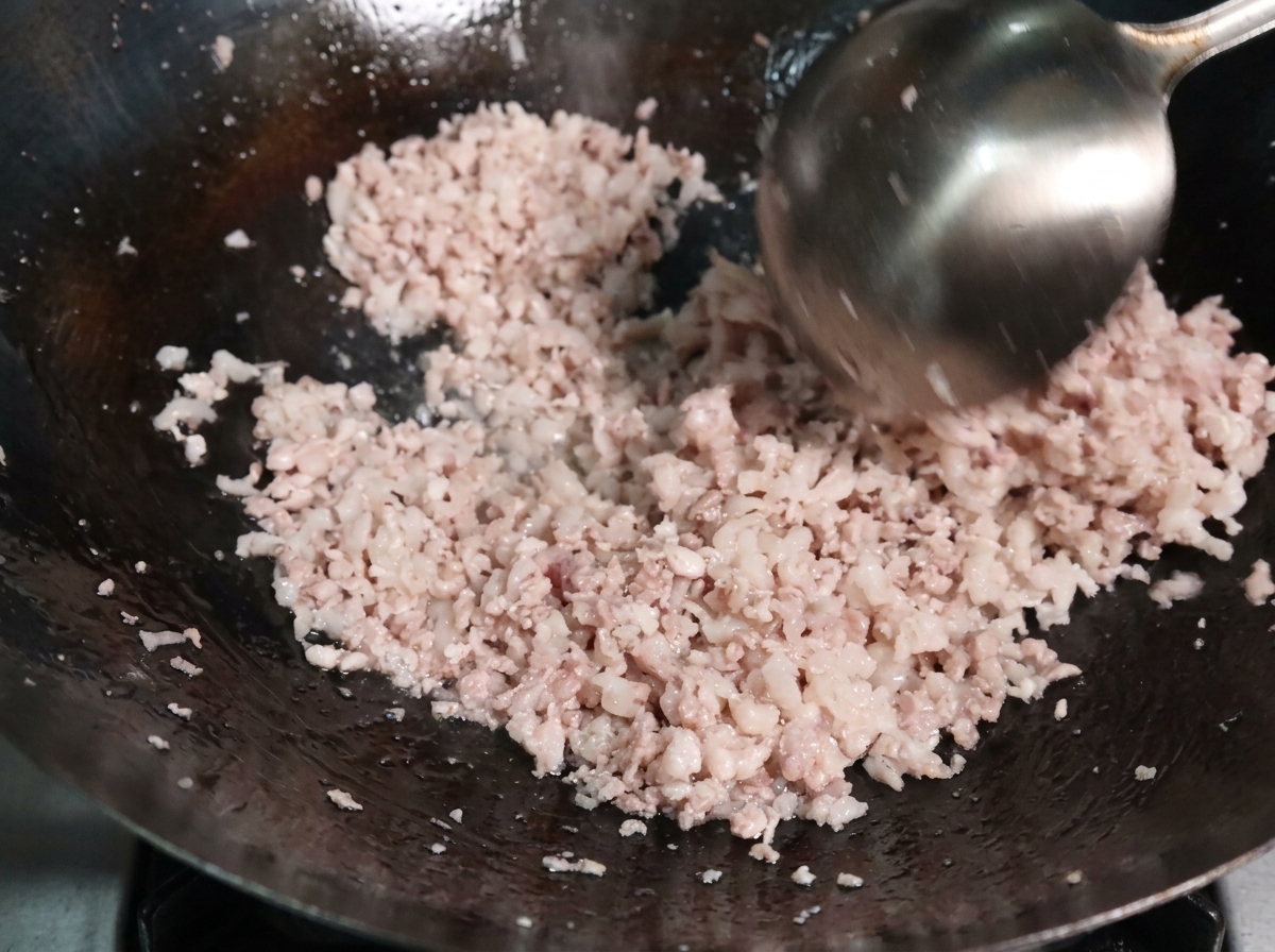 Carne picada siendo salteada con un cucharón en un wok caliente, separándose en granos pequeños al cocinarse.