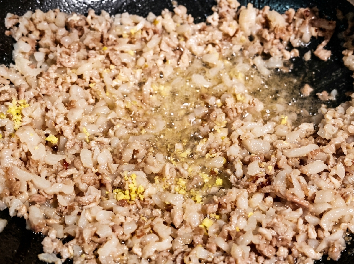 Trozos de ajo y jengibre picados salteándose junto a la carne dorada en un wok oscuro.