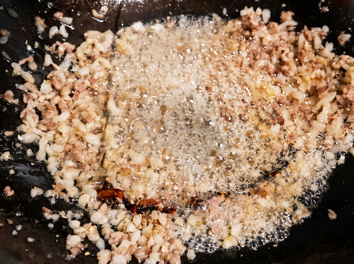 Salsa de soja ligera vertiéndose en un wok con carne salteada, burbujeando sobre el aceite caliente.