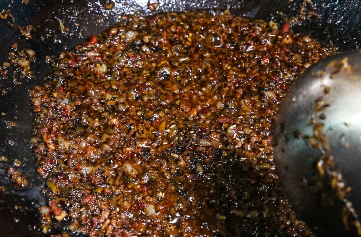 Oscura y sabrosa mezcla de carne y brotes vegetales siendo removida con un cucharón en el wok tras agregar las especias.