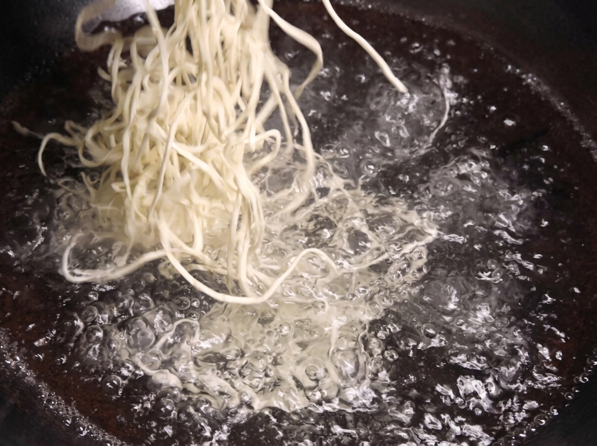 Un manojo de fideos blancos frescos sumergiéndose en una olla con agua hirviendo a borbotones.