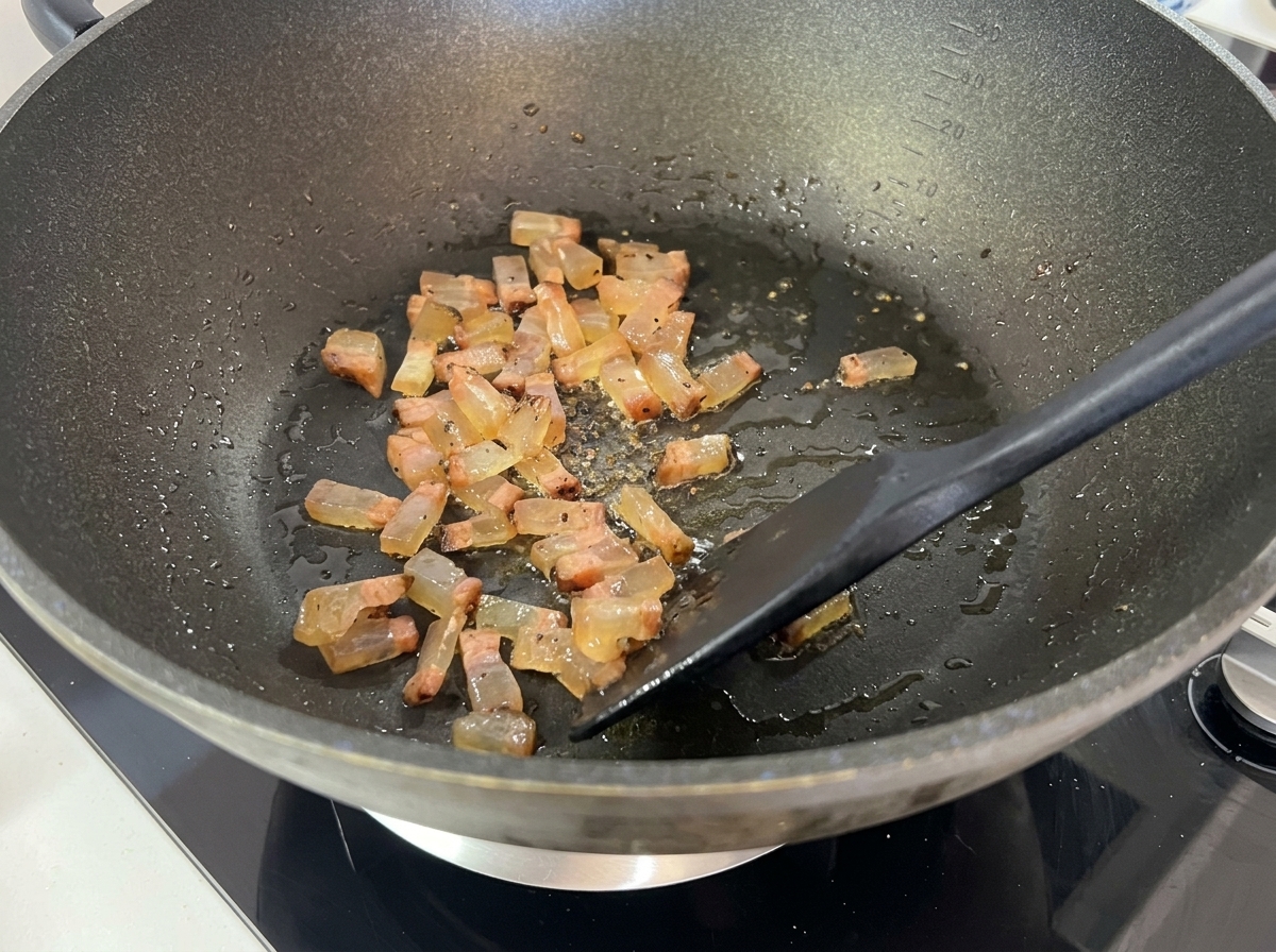 Dados de guanciale dorándose y volviéndose translúcidos en un wok, soltando grasa líquida.