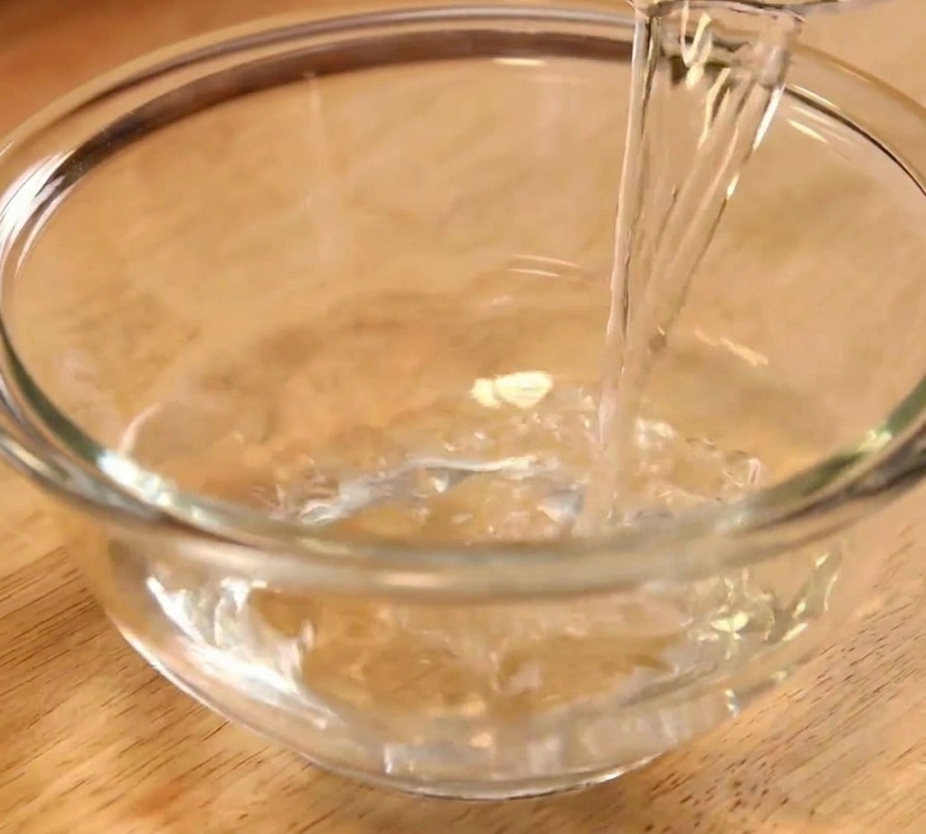 Agua limpia vertiéndose en un tazón de vidrio transparente como primer paso para la preparación de la salsa.