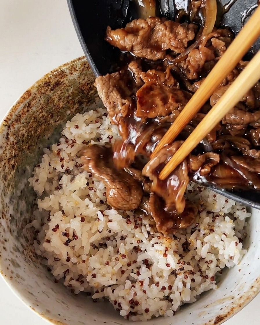 Ternera y cebollas cocinadas vertiéndose desde una sartén sobre un bol de arroz blanco al vapor mezclado con quinoa.