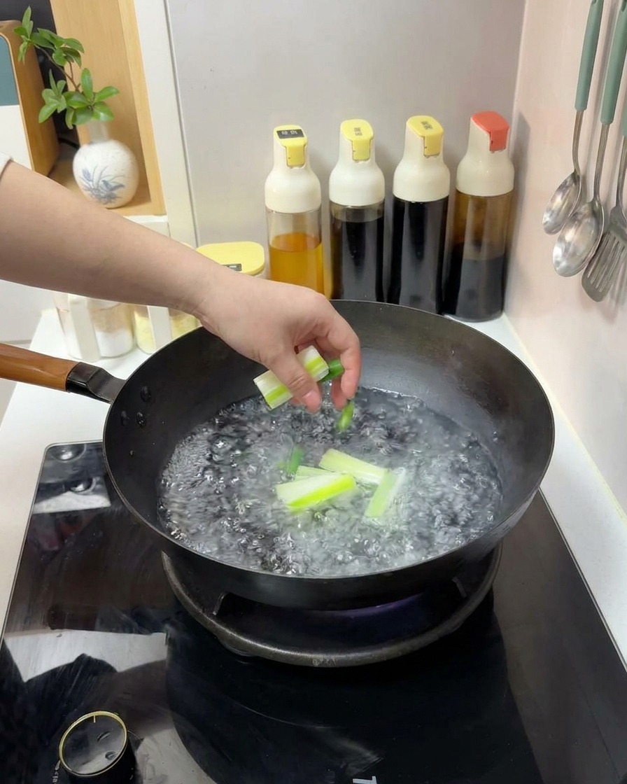 Una mano dejando caer trozos cortados de cebolleta verde en un wok con agua hirviendo.