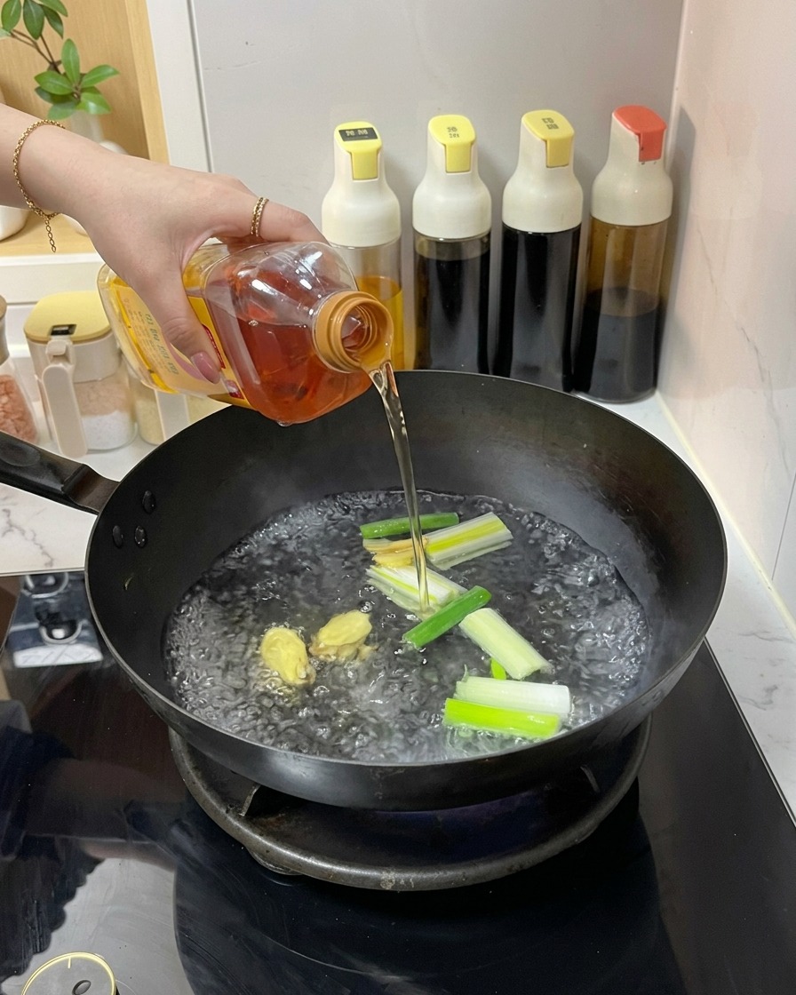 Una persona vertiendo un líquido ámbar transparente desde una botella de plástico en un wok con agua hirviendo, jengibre y cebolletas.