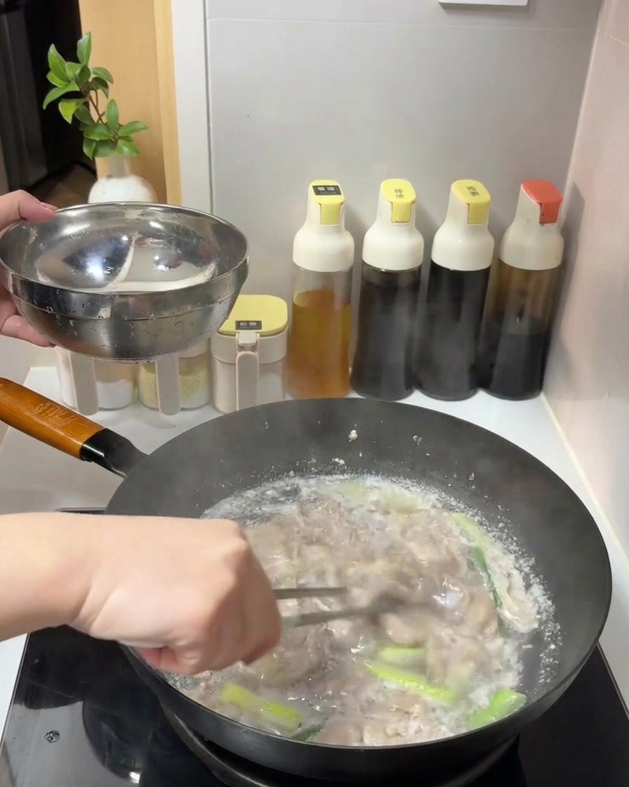 Láminas de ternera cocinada siendo retiradas con pinzas de una olla de agua hirviendo hacia un tazón de metal.