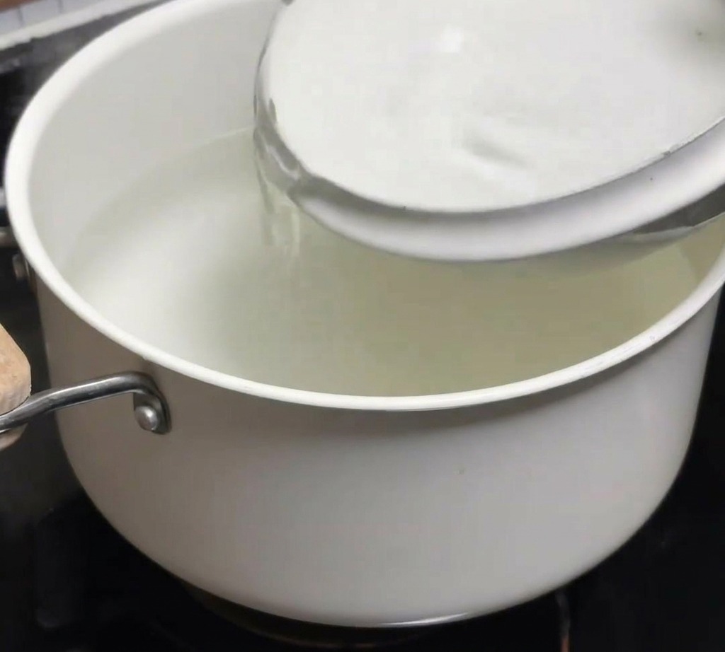 Un tazón de agua fría vertiéndose en una olla de agua caliente recién hervida.
