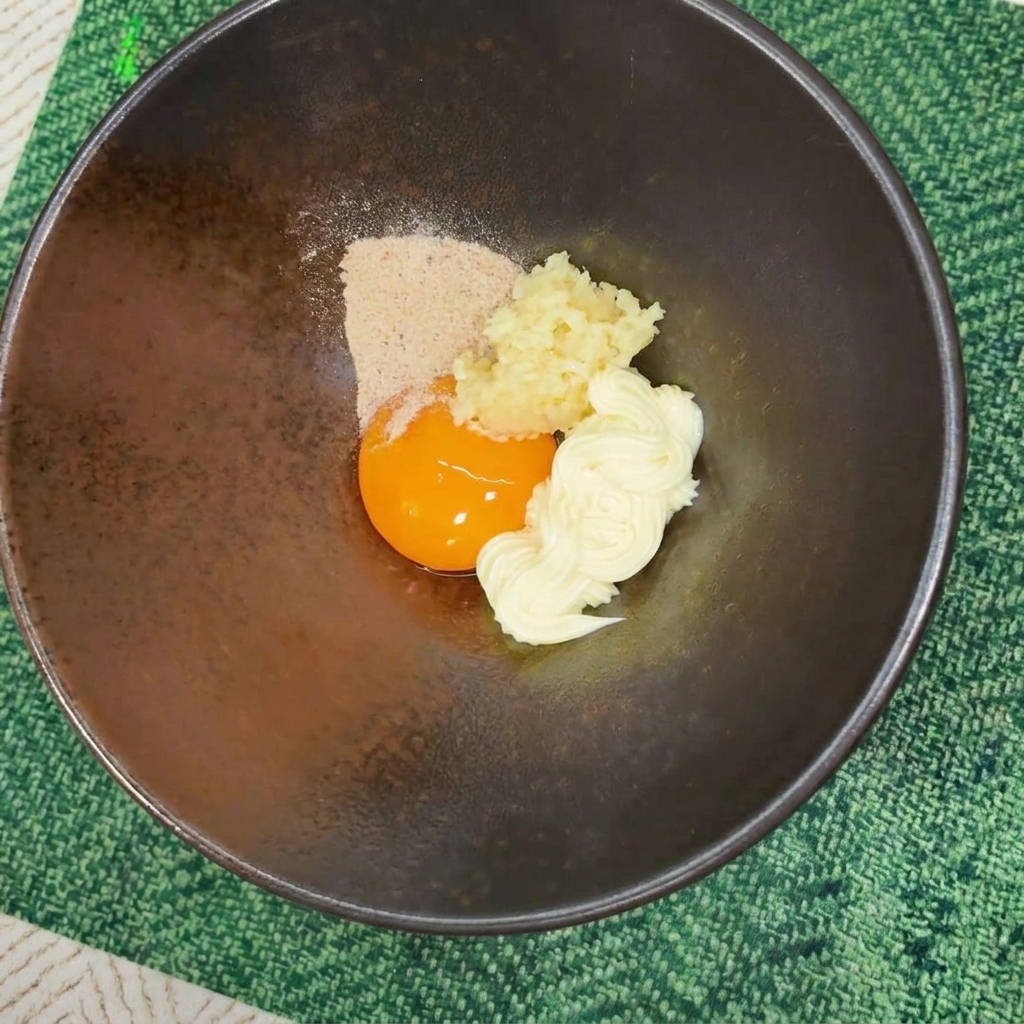 Polvo de condimento vertido sobre la yema de huevo, la mayonesa y el ajo picado en un cuenco oscuro.